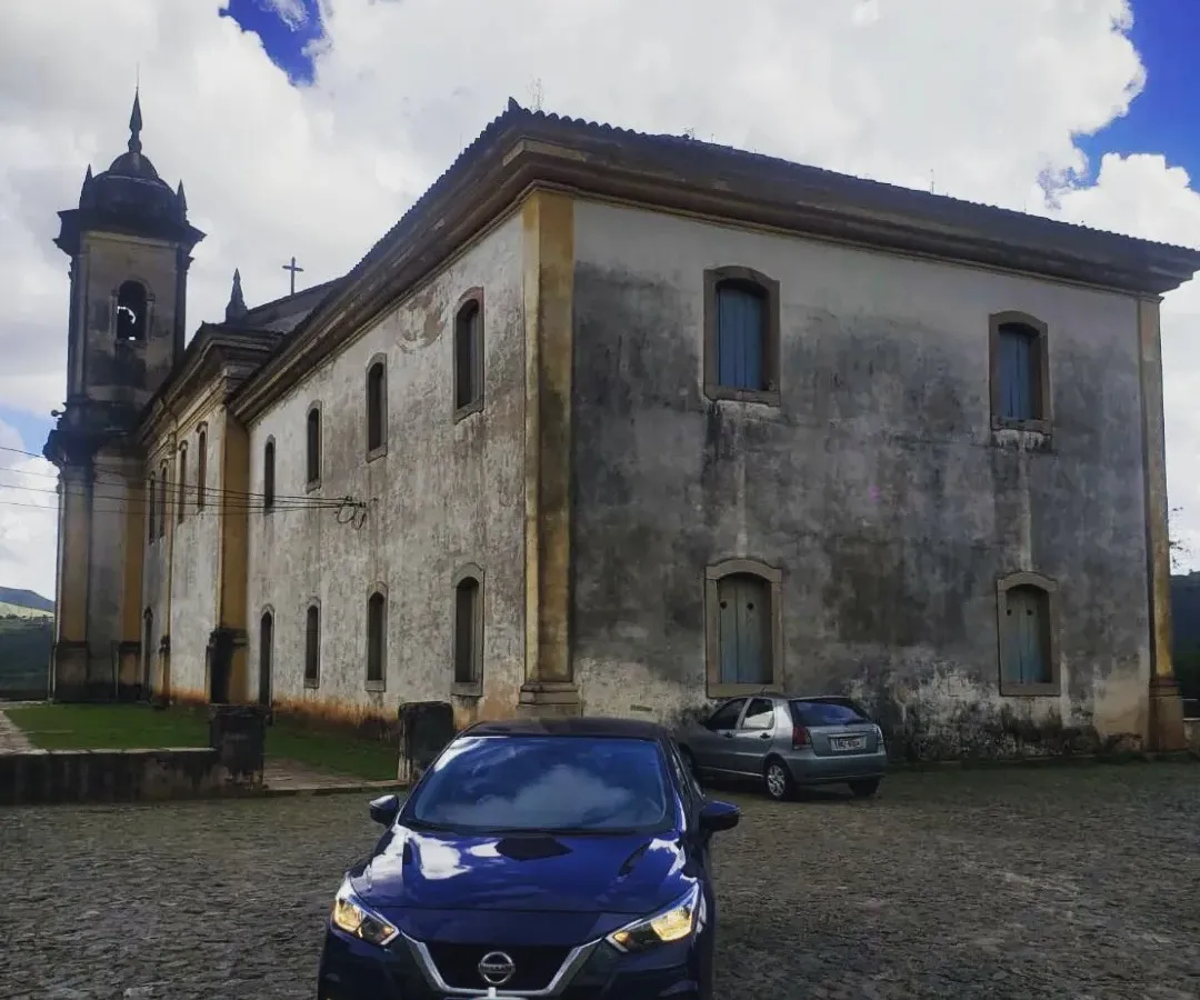 Sedan azul da VD Transportes diante de igreja barroca no centro histórico de Ouro Preto